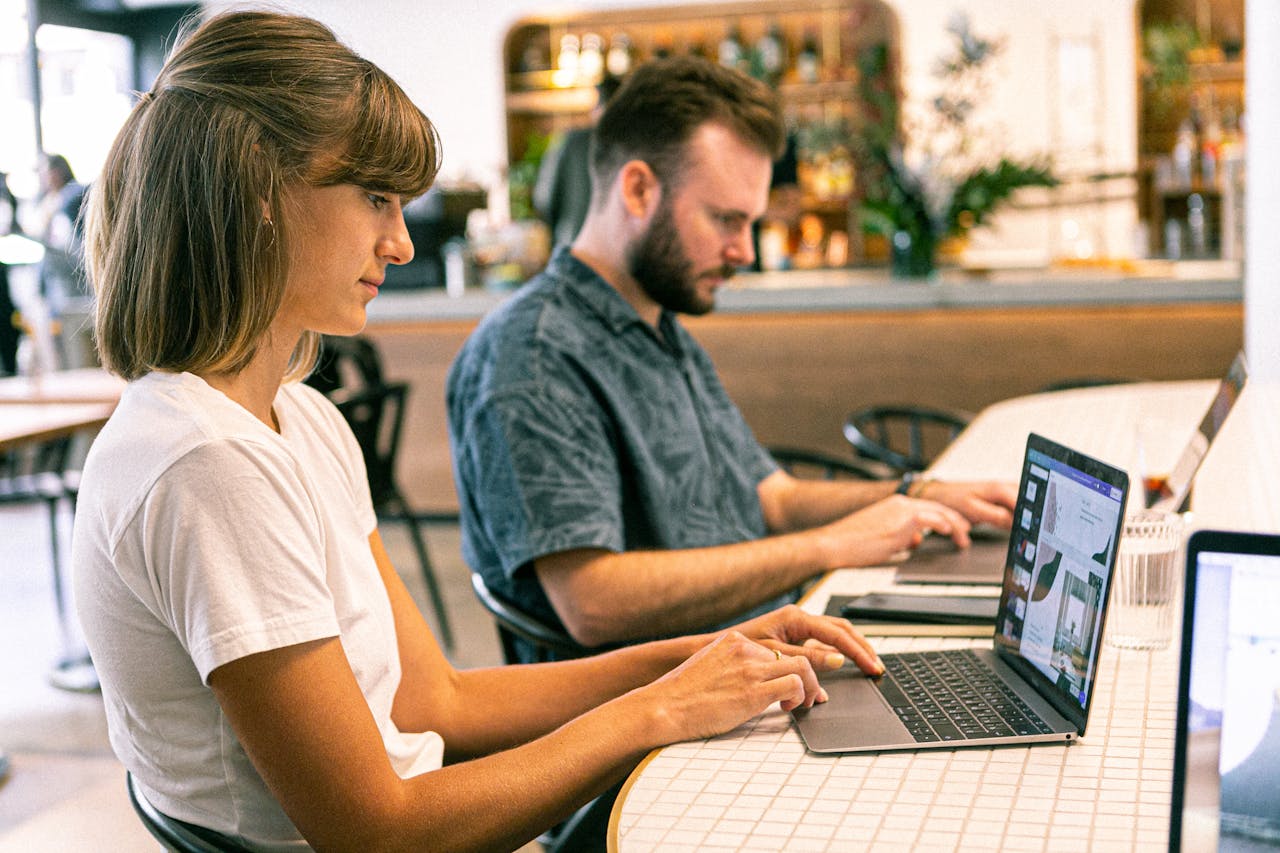 about-us Two young professionals working on laptops in a modern cafe setting.